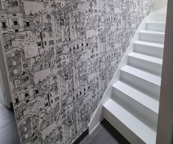 Pose d’un papier peint noir et blanc à motifs urbains dans une cage d’escalier à Brest.