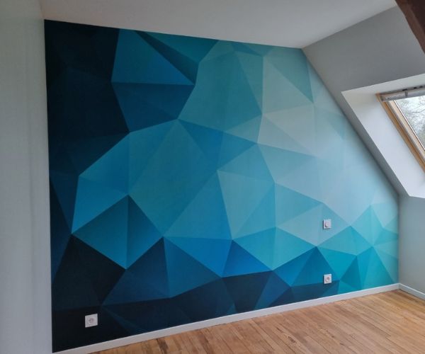 Pose d’un papier peint panoramique bleu géométrique dans une chambre à Brest par Ouest Déco.